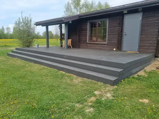 Pelēka kompozīta terase ar pakāpieniem pie koka mājas